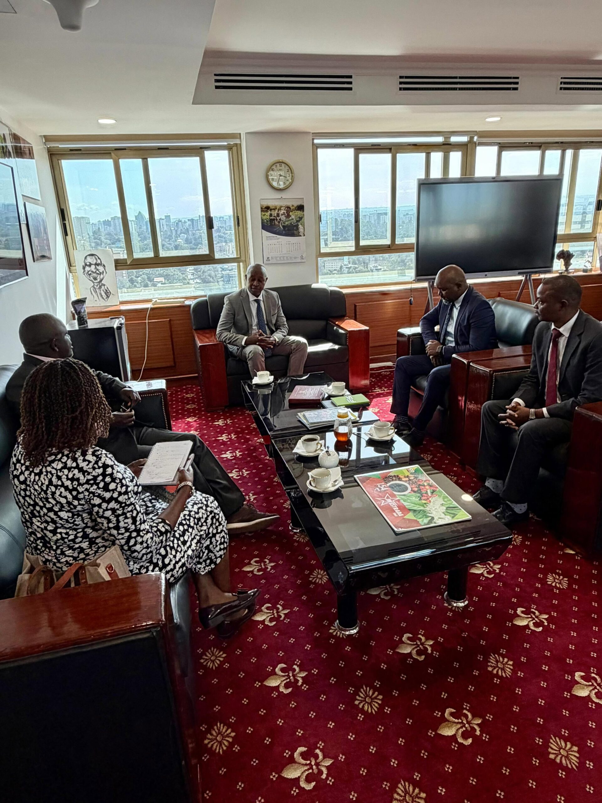 Group of professionals in suits seated around a glass coffee table in a high-rise office, city skyline visible through large windows.