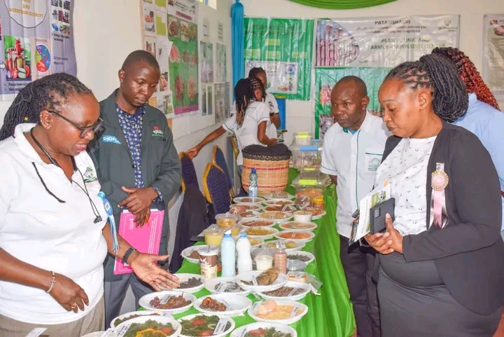 A group of people at a food expo examining a long table filled with various plated dishes and drinks.