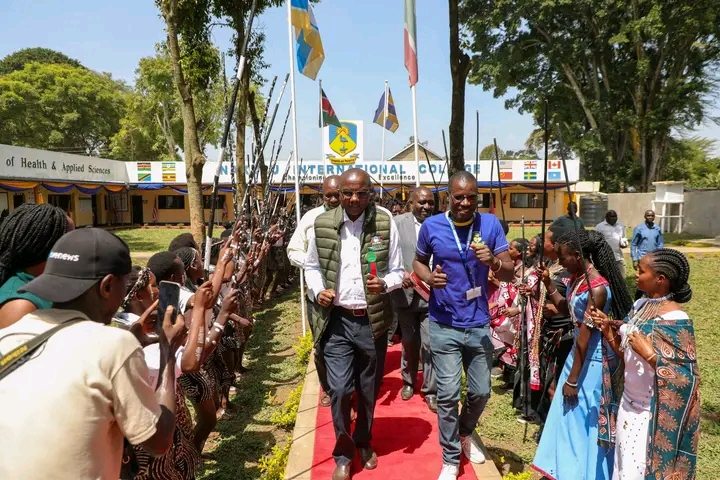 Formal visitors walk a red carpet flanked by students and ceremonial guards as flags fly overhead at an international college campus event.
