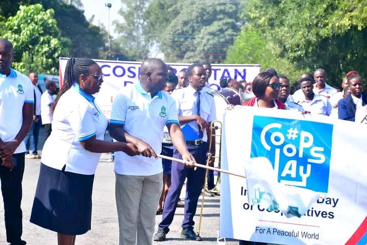 Group of people in matching white and light blue uniforms participate in an outdoor ceremony, holding a banner and a poster that reads '#OPS DAY'.