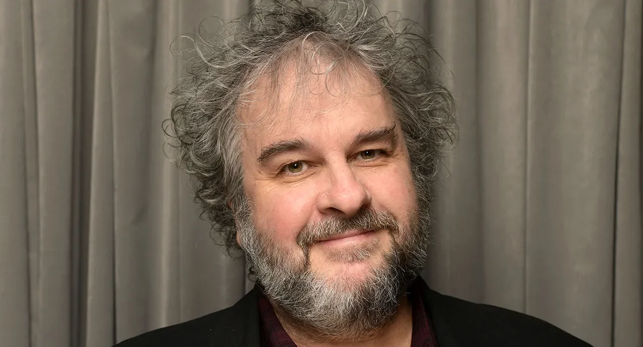 What Is Peter Jackson Net Worth? - Sacco Trend Magazine Smiling middle-aged man with gray hair and a salt-and-pepper beard, wearing a dark blazer in front of gray curtains.