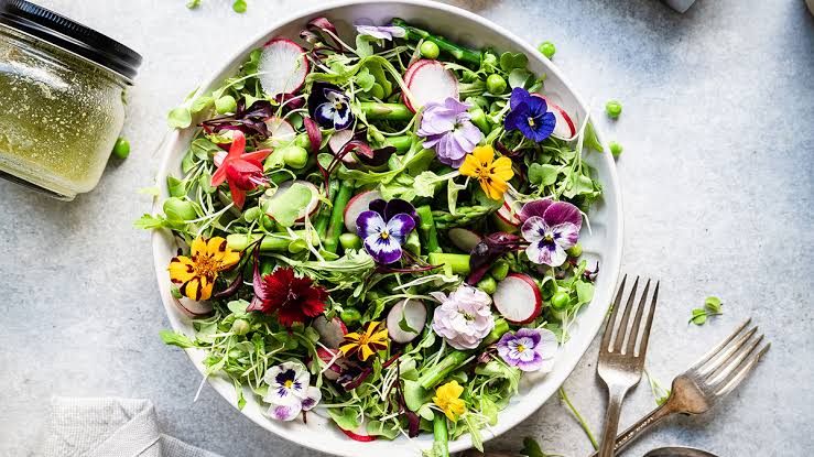 images - 2026-08-05T073414376 - Sacco Trend Magazine Colorful salad with edible flowers in a white bowl, radishes and greens; a dressing jar nearby on the table.
