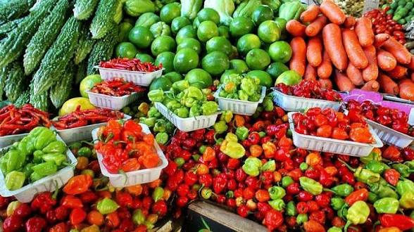 Colorful market display of peppers, limes, and cucumbers with small baskets of red and green peppers in the foreground.