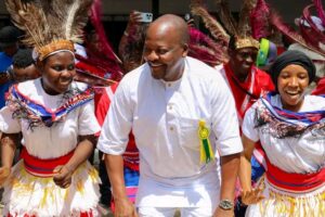 1788504446596 - Sacco Trend Magazine Man in white dancing among performers wearing colorful traditional outfits and feathered headpieces at a cultural celebration, smiling broadly.