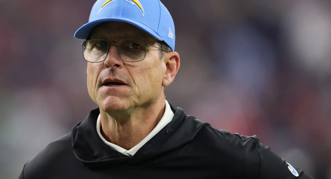 Close-up of a man wearing a light-blue Chargers cap and glasses, looking to the side in a stadium setting.