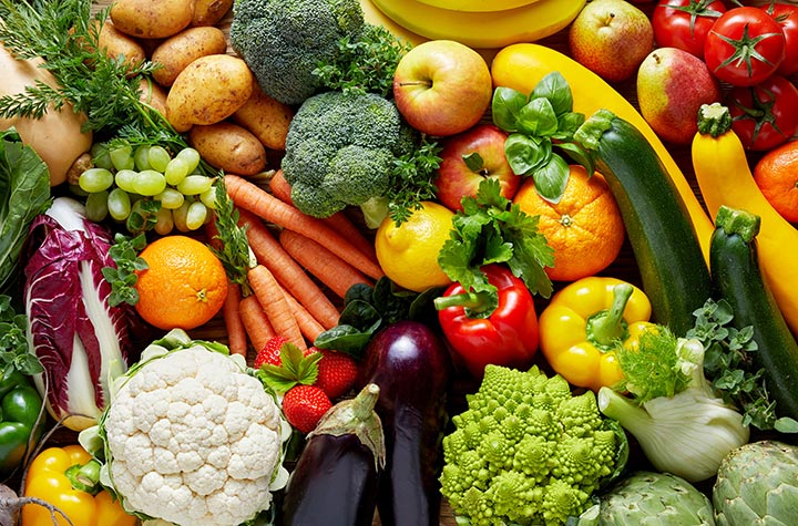 Colorful produce spread with carrots, broccoli, cauliflower, leafy greens, peppers, apples, and squash.