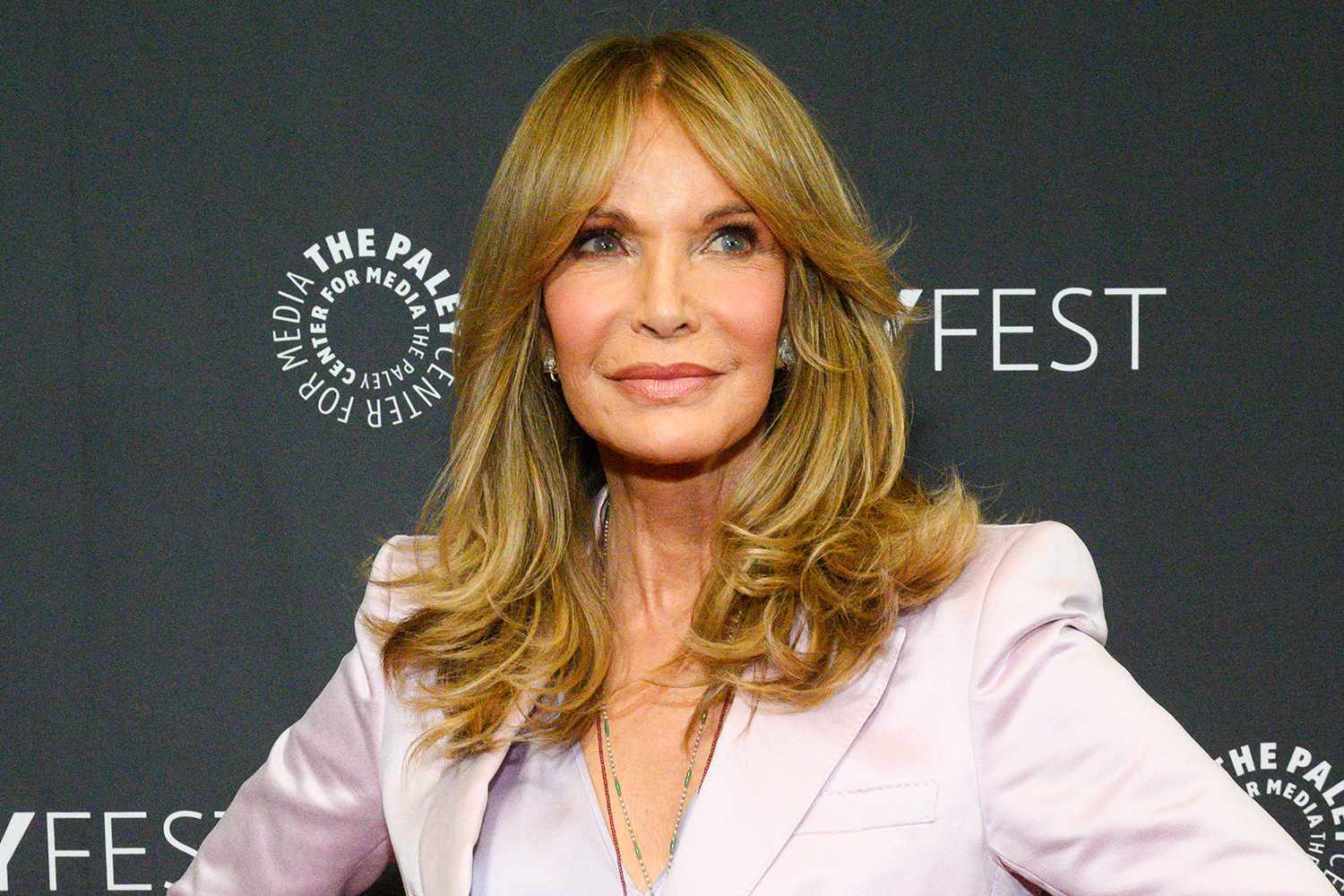 Blonde woman on a red carpet at PaleyFest, wearing a pale pink blazer and layered hair.