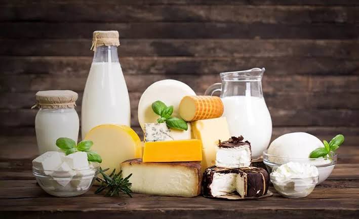 Assorted dairy products on a wooden table: bottles of milk, cheeses, butter, cream, yogurt, and a milk jug.
