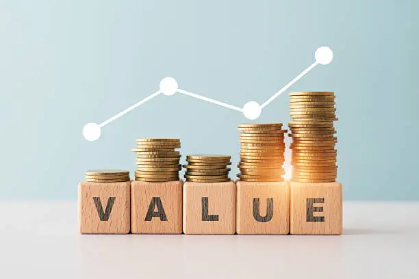 Stacks of coins rise on wooden blocks spelling VALUE, with a white line graph showing growth.