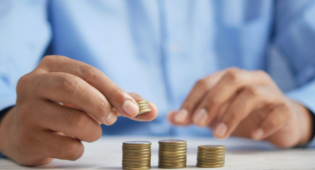 Close-up of hands stacking coins into small towers on a table surface
